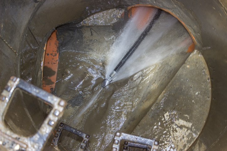 image of a hose inserted into a drain spraying a jet of water.